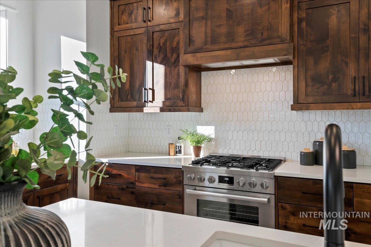Kitchen with stainless steel range with gas stovetop, backsplash, dark brown cabinetry, and under cabinet range hood