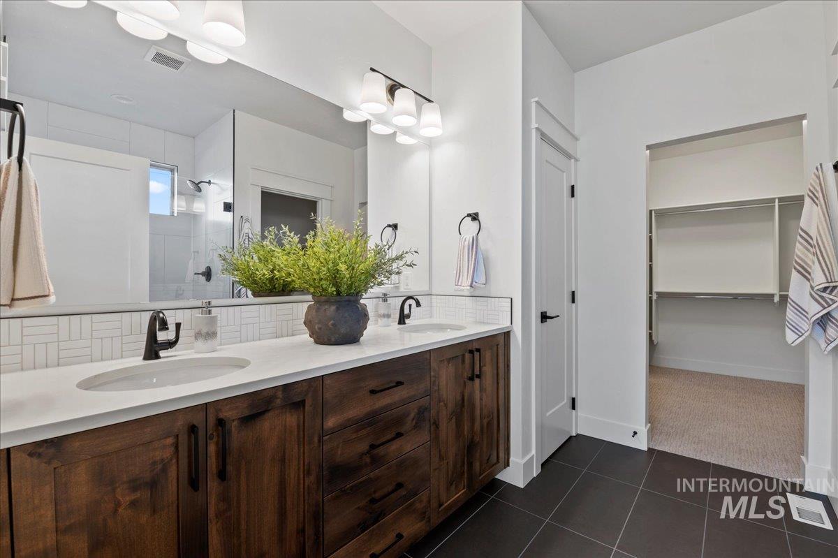 Full bath featuring dark tile patterned floors, double vanity, a shower stall, a walk in closet, and tasteful backsplash