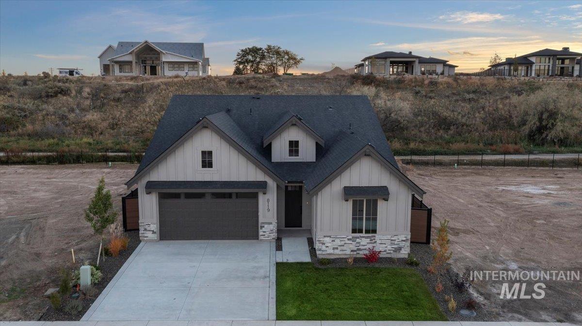 Modern inspired farmhouse featuring board and batten siding, driveway, stone siding, and roof with shingles
