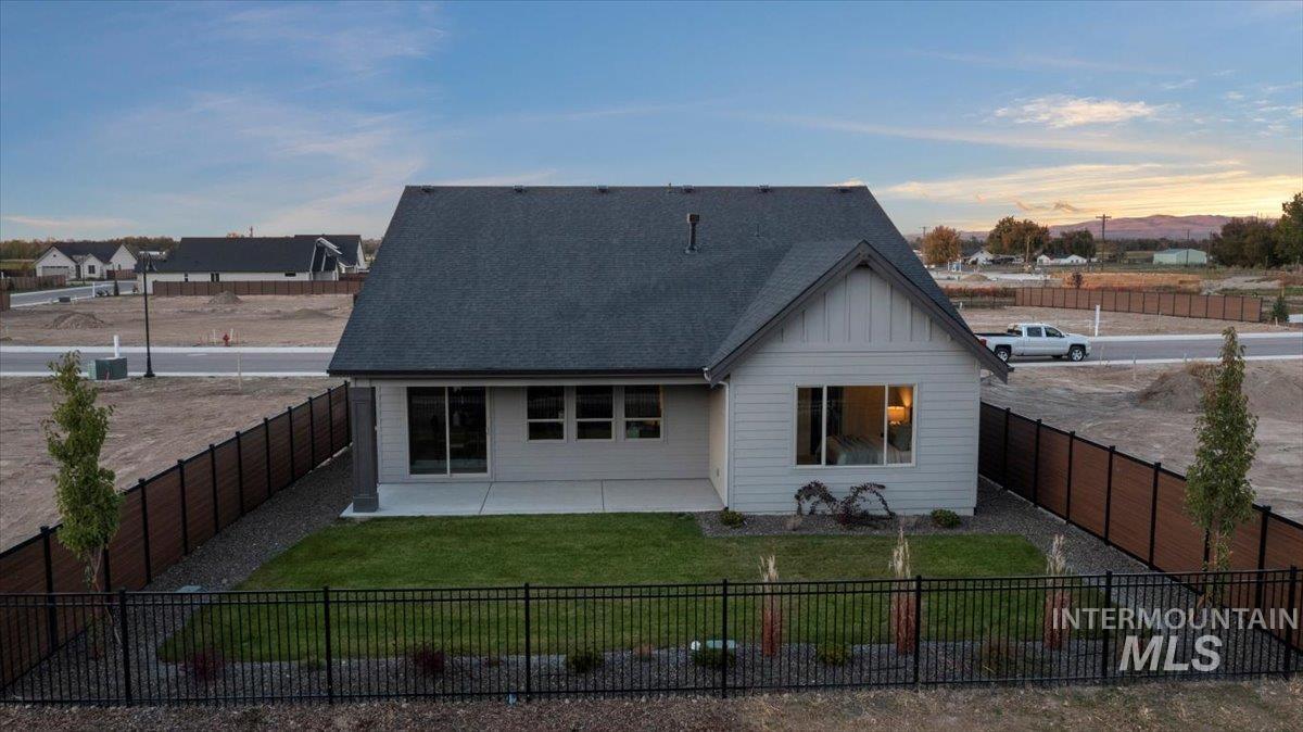Rear view of property featuring board and batten siding, a fenced backyard, a shingled roof, and a patio