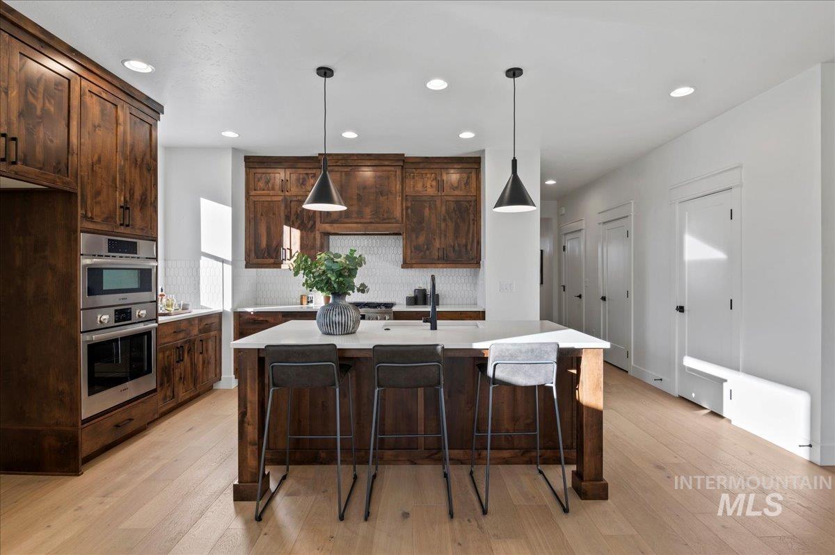 Kitchen featuring dark brown cabinets, a kitchen breakfast bar, light wood finished floors, hanging light fixtures, and recessed lighting
