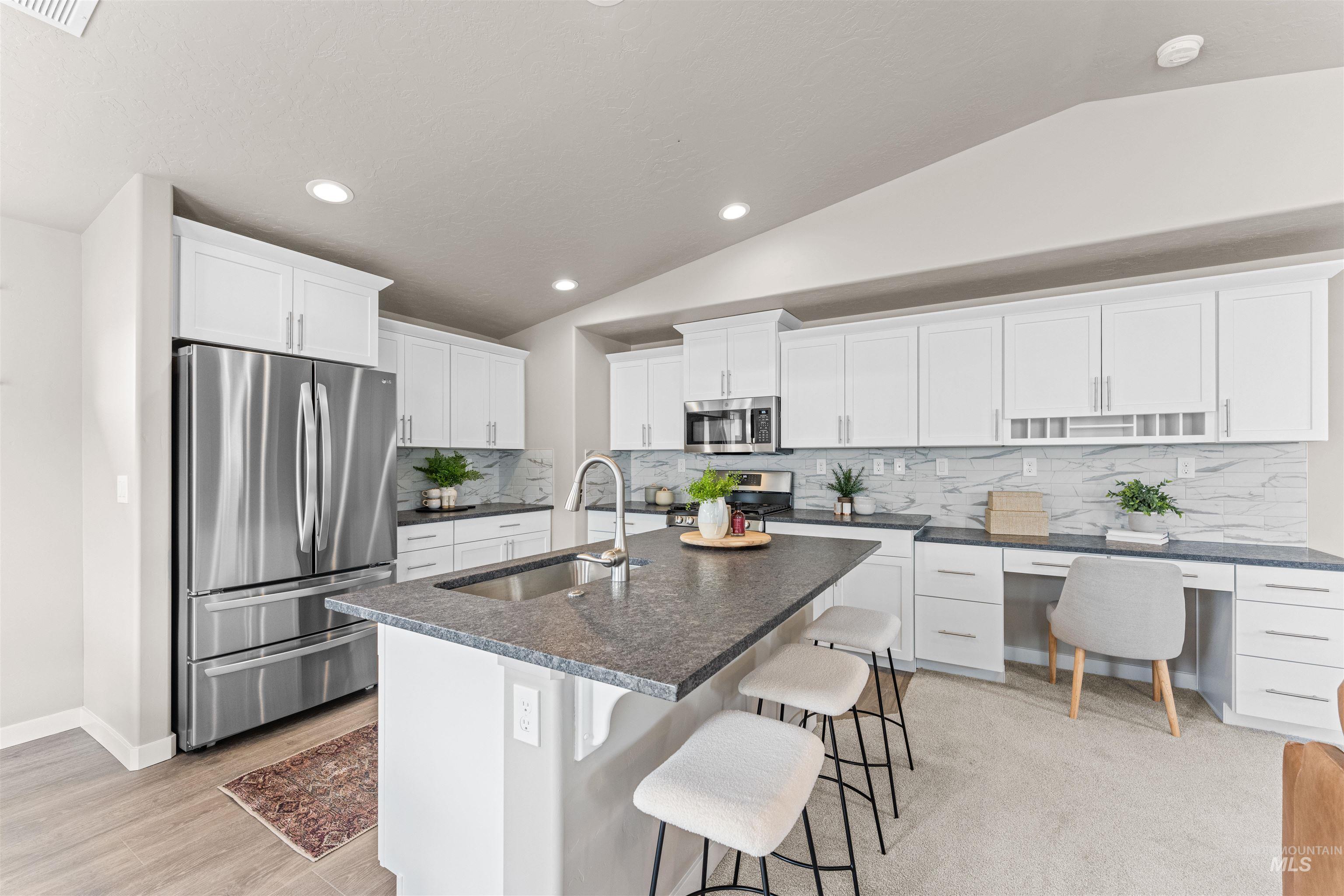 Kitchen featuring decorative backsplash, stainless steel appliances, lofted ceiling, white cabinets, and a center island with sink