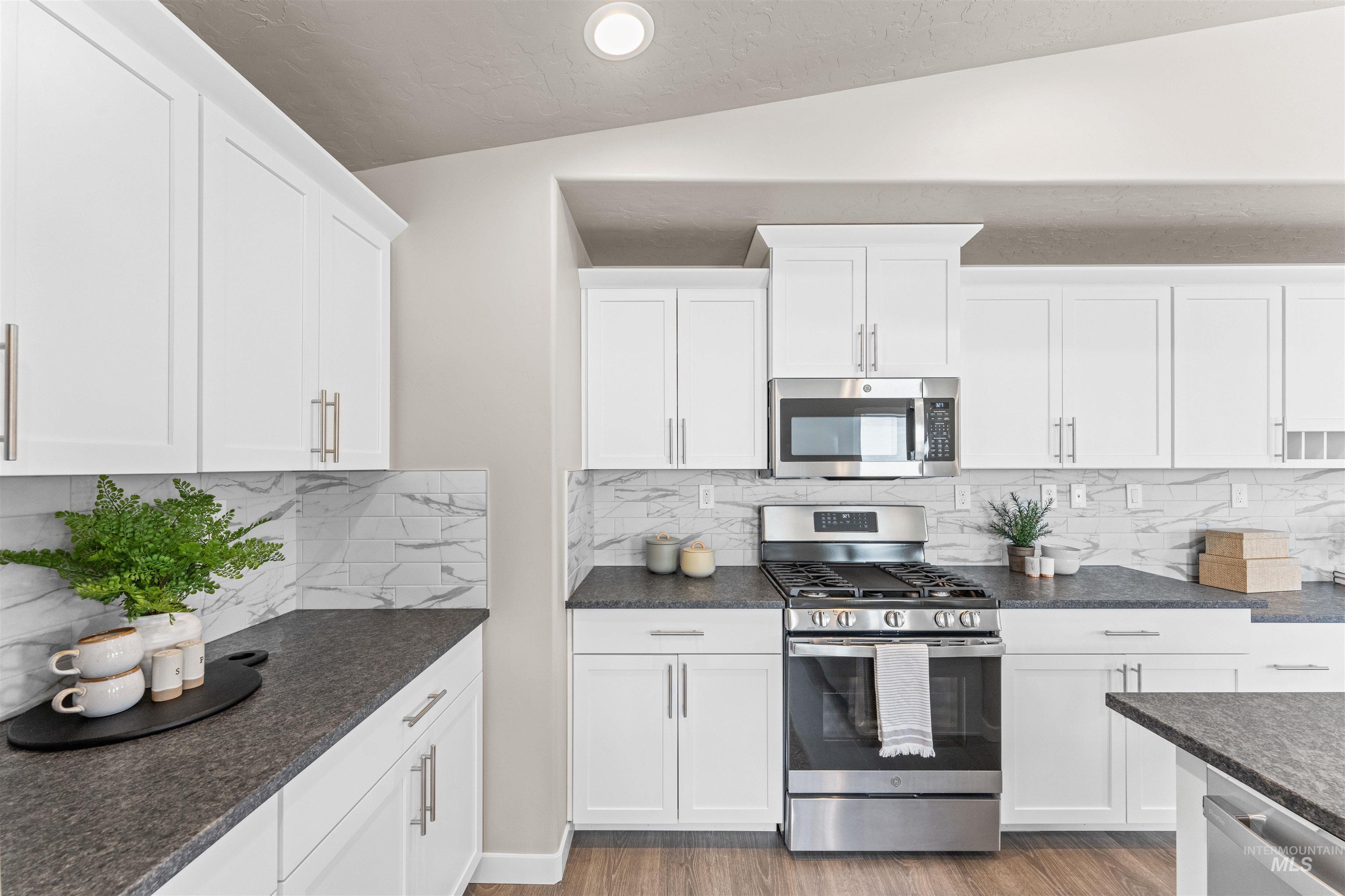Kitchen with stainless steel appliances, backsplash, white cabinets, dark stone countertops, and vaulted ceiling