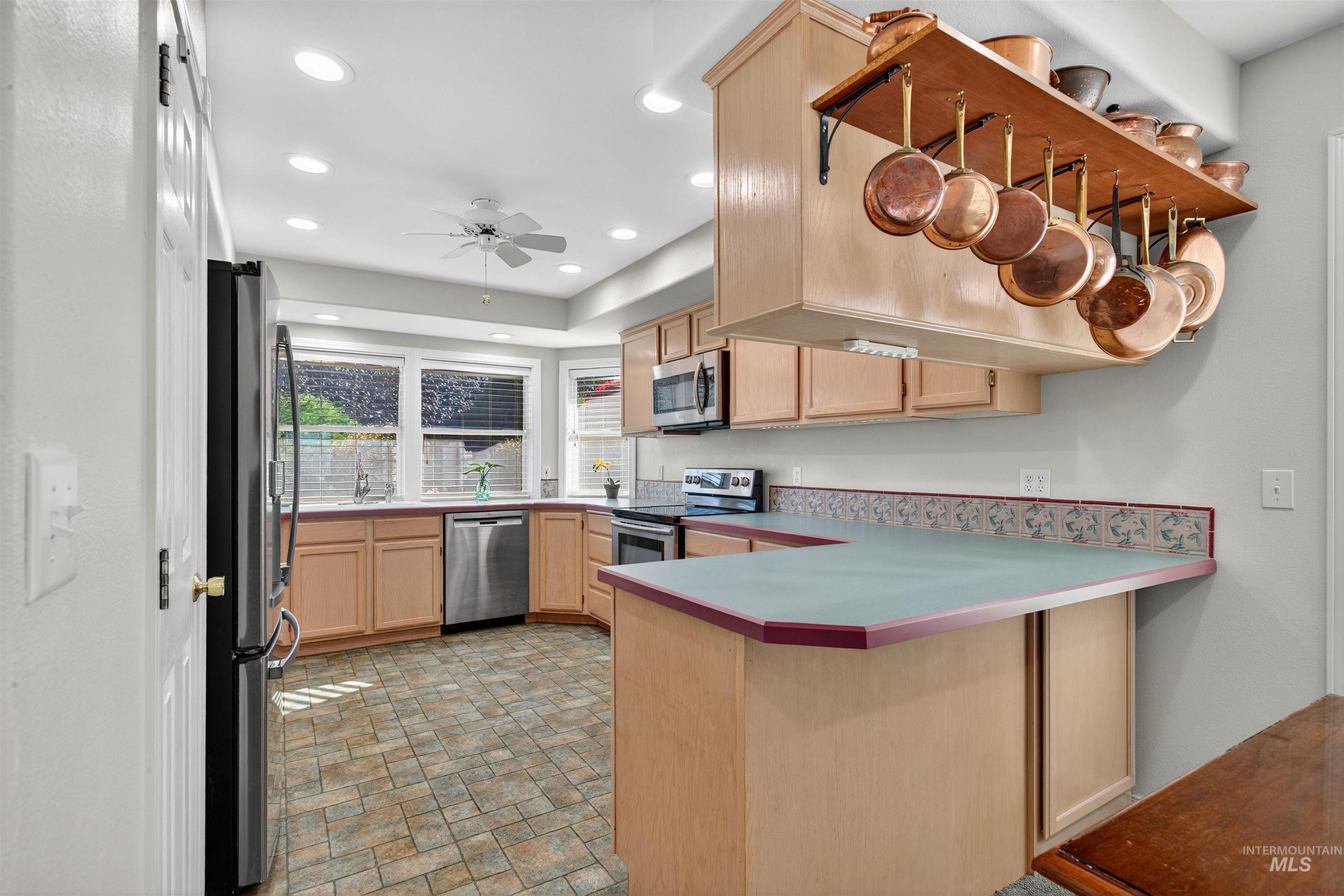 Kitchen featuring light brown cabinets, a peninsula, stone finish flooring, stainless steel appliances, and a ceiling fan