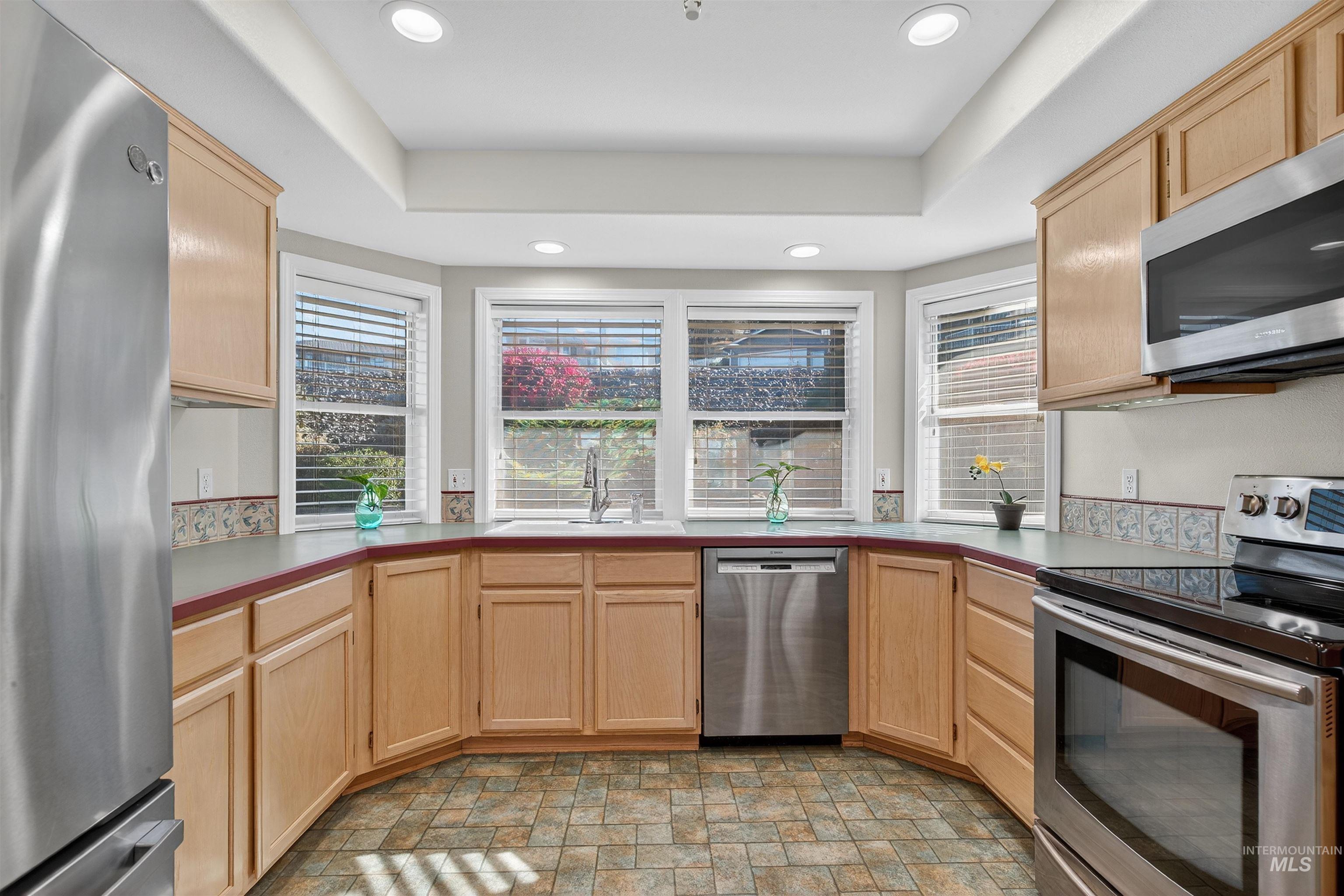 Kitchen with light brown cabinetry, stainless steel appliances, stone finish flooring, recessed lighting, and light countertops
