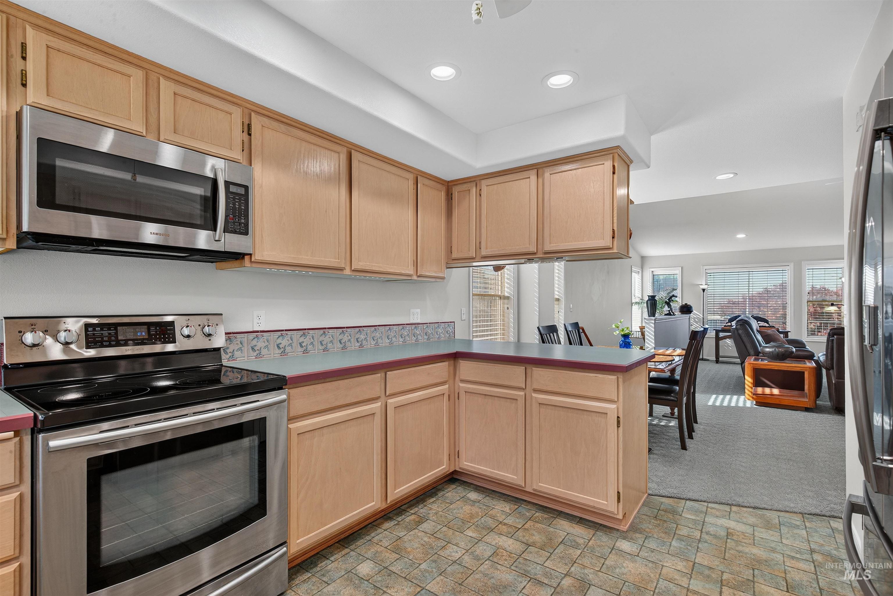 Kitchen with light brown cabinetry, stainless steel appliances, recessed lighting, a peninsula, and light carpet