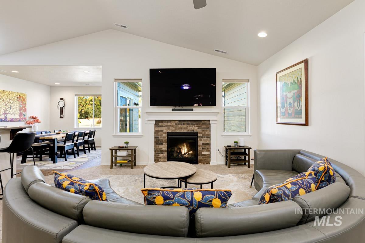 Carpeted living room with a warm lit fireplace, vaulted ceiling, recessed lighting, and a ceiling fan