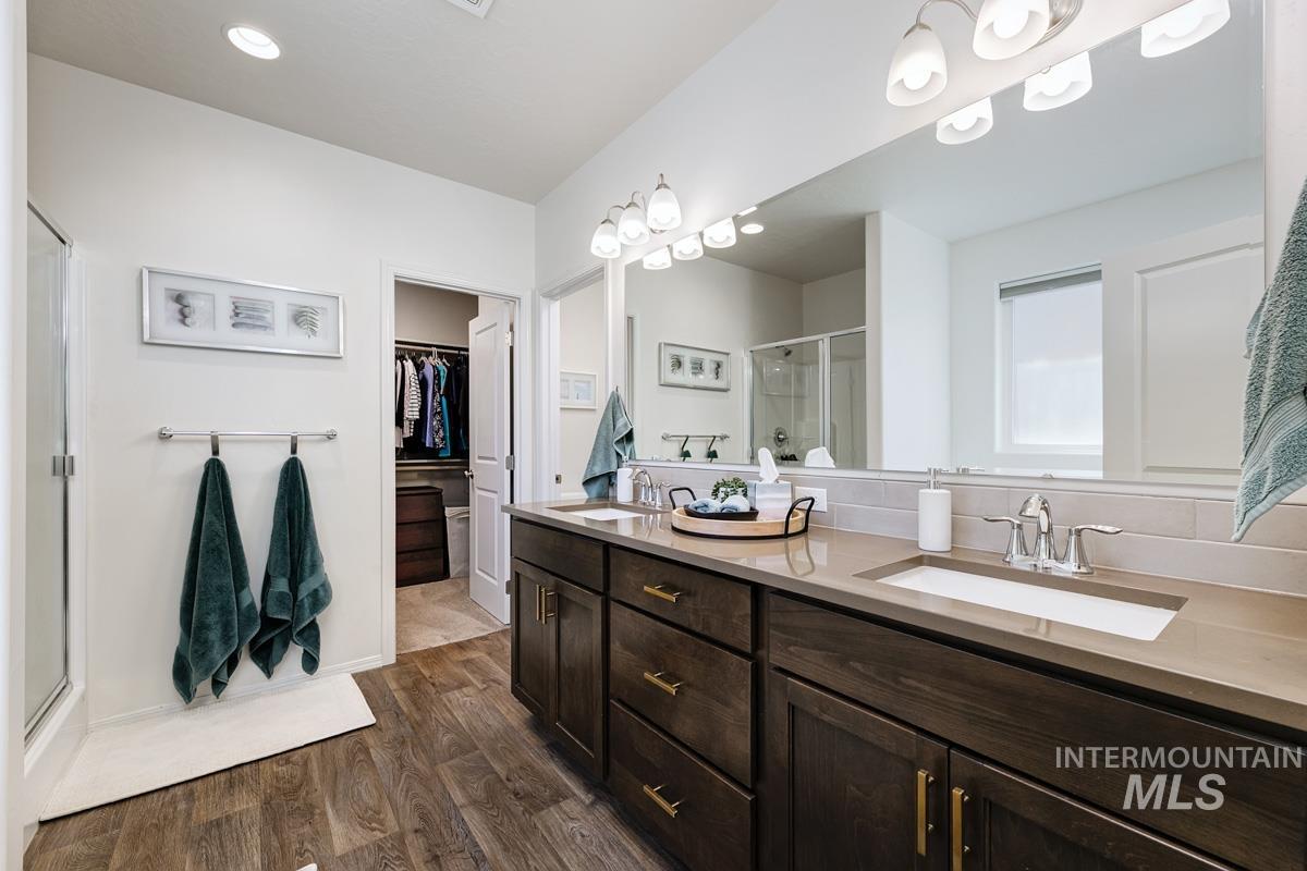 Bathroom featuring a stall shower, double vanity, dark wood-style flooring, a spacious closet, and recessed lighting