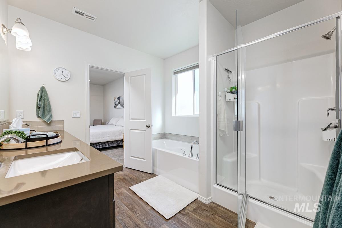 Ensuite bathroom with dark wood-style flooring, a stall shower, a bath, and double vanity