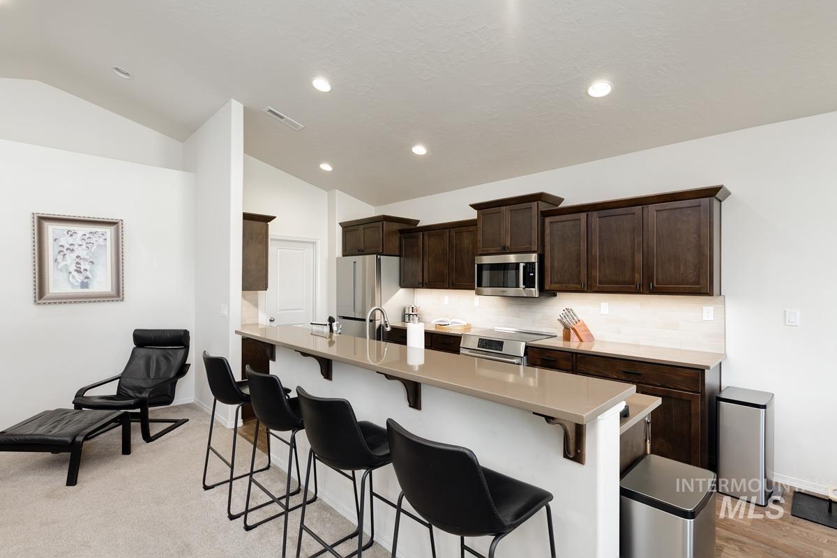 Kitchen featuring dark brown cabinets, a breakfast bar area, vaulted ceiling, decorative backsplash, and recessed lighting