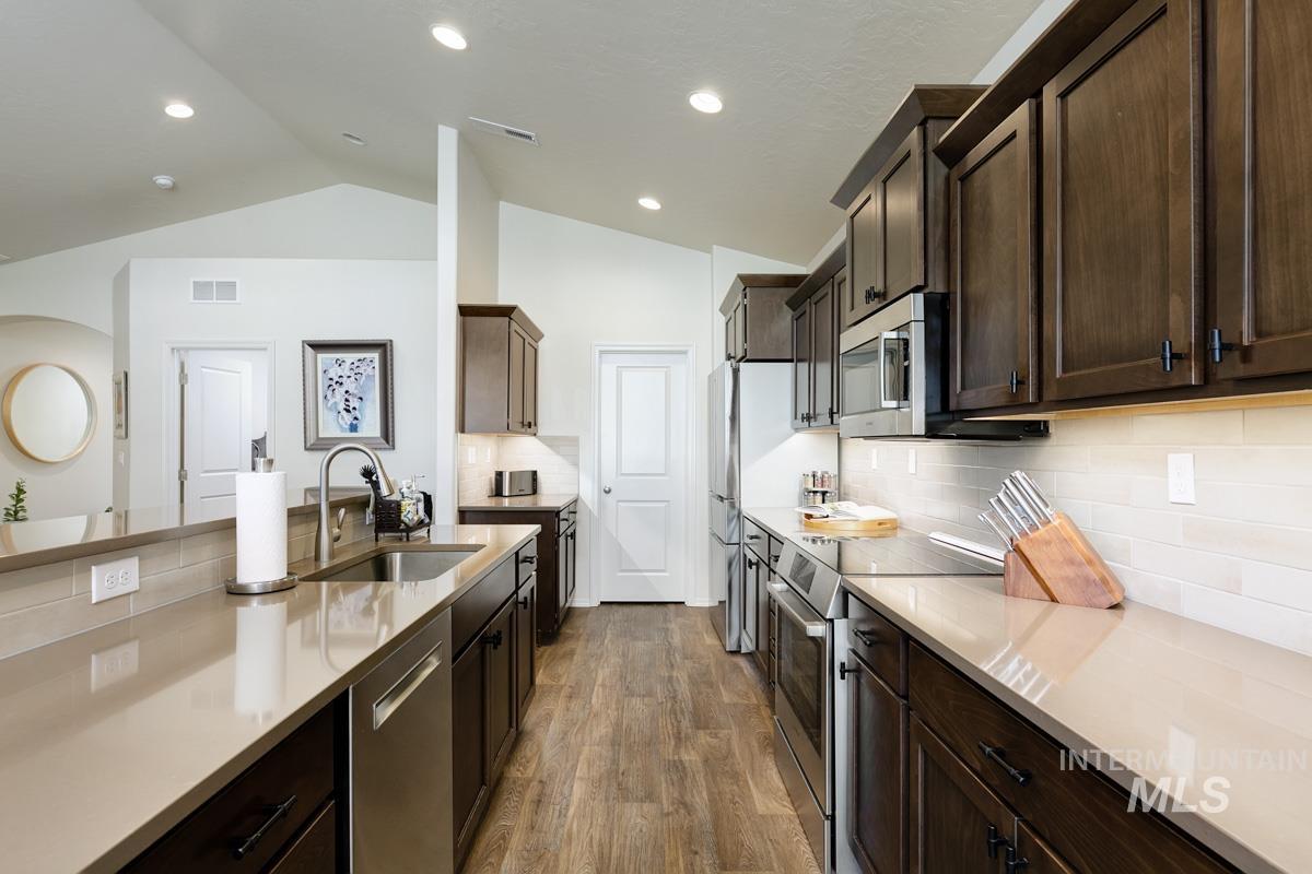 Kitchen with appliances with stainless steel finishes, dark wood-style flooring, dark brown cabinetry, lofted ceiling, and decorative backsplash
