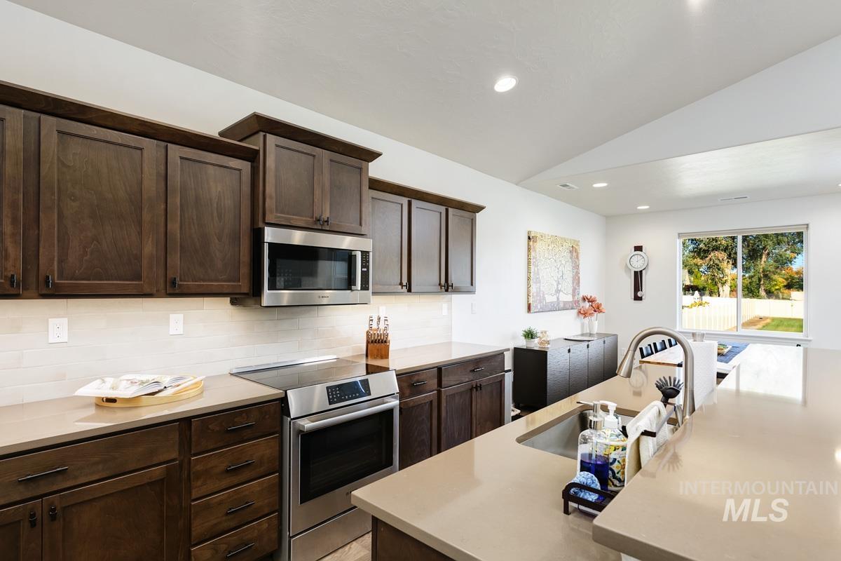 Kitchen with appliances with stainless steel finishes, vaulted ceiling, dark brown cabinets, recessed lighting, and decorative backsplash