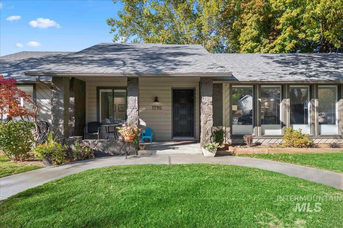 Doorway to property with a lawn, roof with shingles, and a porch