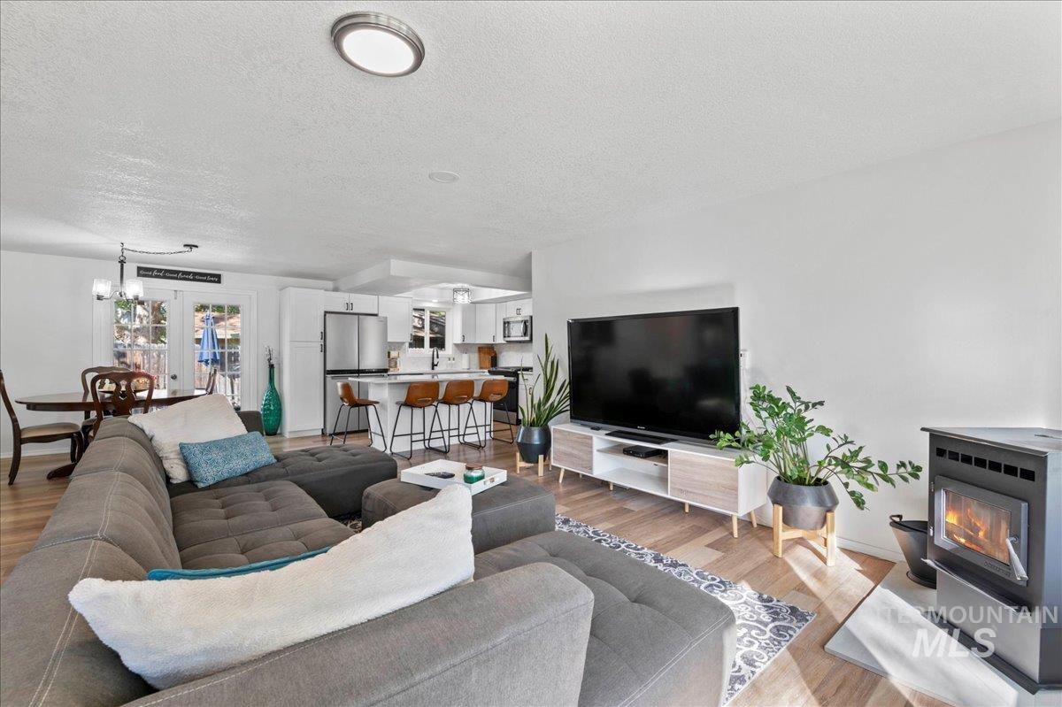 Living area with a wood stove, light wood finished floors, a textured ceiling, and a chandelier