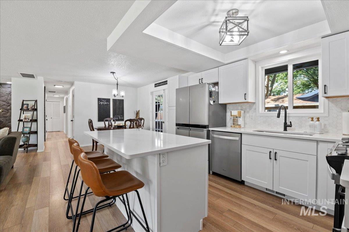 Kitchen with hanging light fixtures, white cabinets, a breakfast bar area, light wood-type flooring, and stainless steel dishwasher