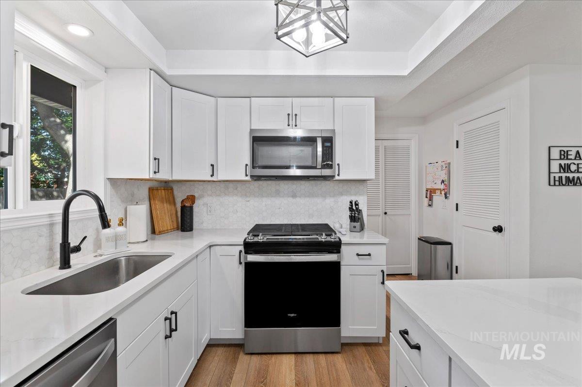 Kitchen featuring white cabinets, stainless steel appliances, backsplash, light stone countertops, and light wood-style floors