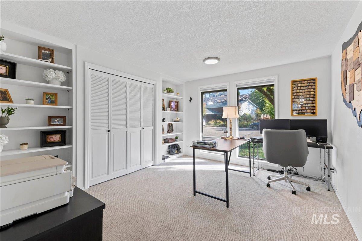 Home office featuring light colored carpet, a textured ceiling, and built in features