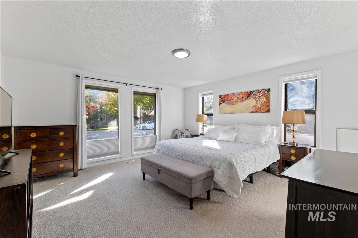 Bedroom with a textured ceiling, light colored carpet, and access to exterior