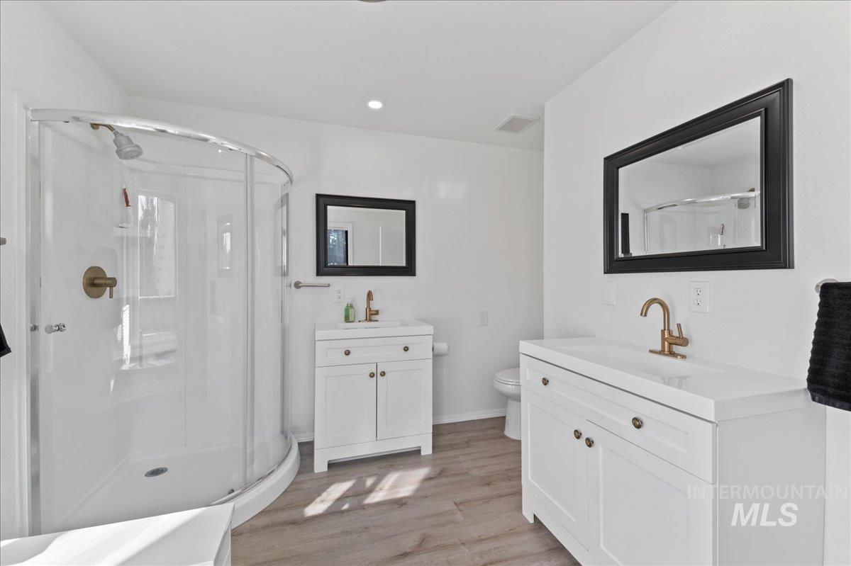 Full bath with two vanities, a shower stall, light wood-style floors, and recessed lighting