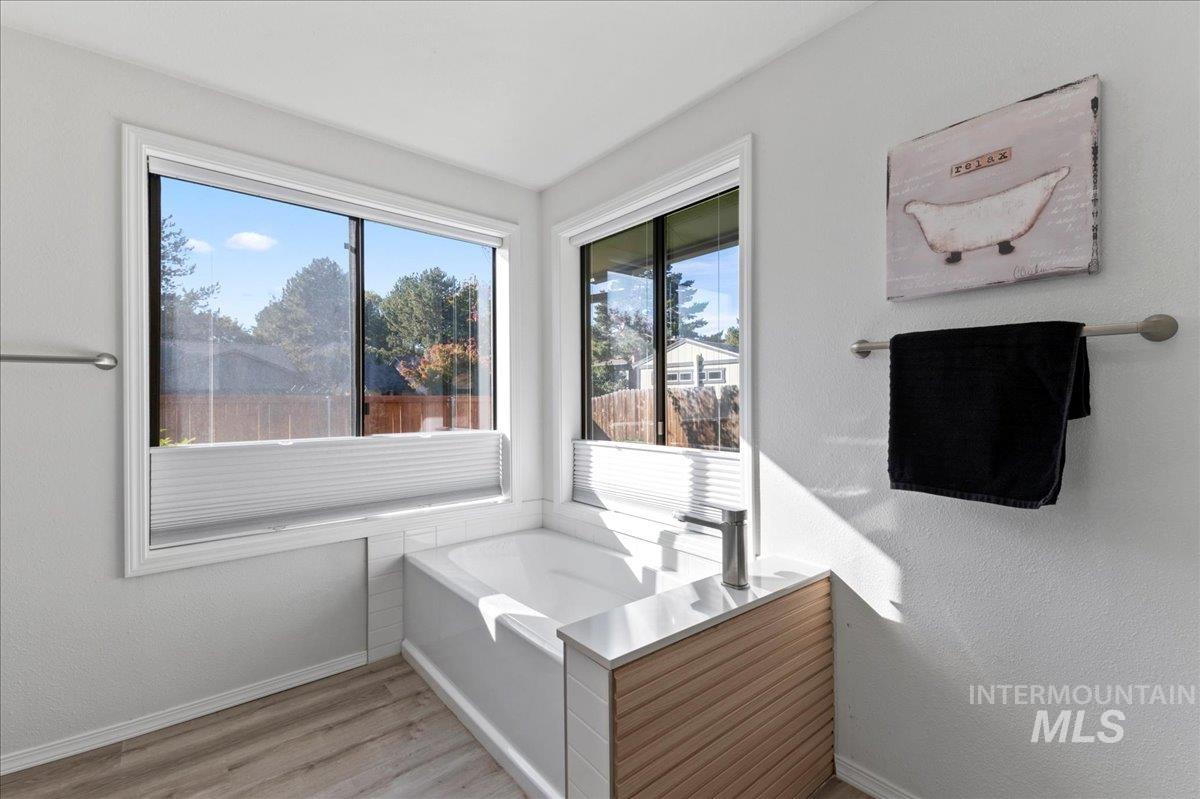 Bathroom featuring a garden tub, light wood-style flooring, and a textured wall
