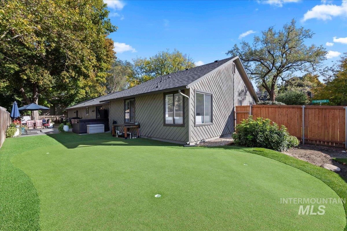 Rear view of property featuring an area to practice putting, a jacuzzi, a fenced backyard, and a patio