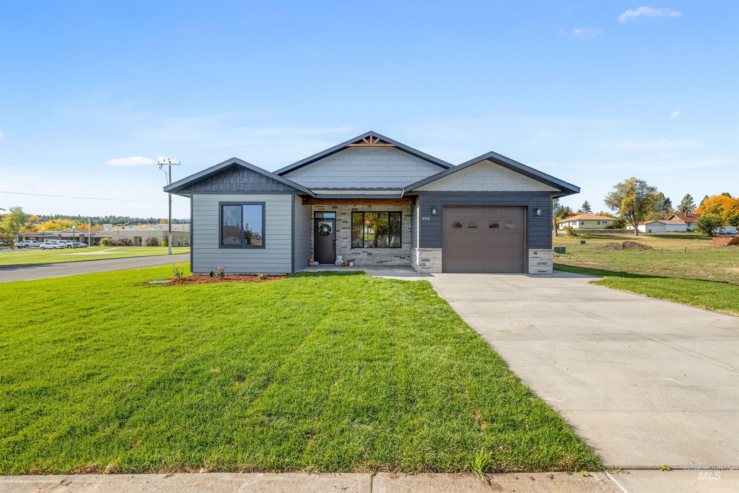 View of front of house with driveway, a front yard, an attached garage, and stone siding