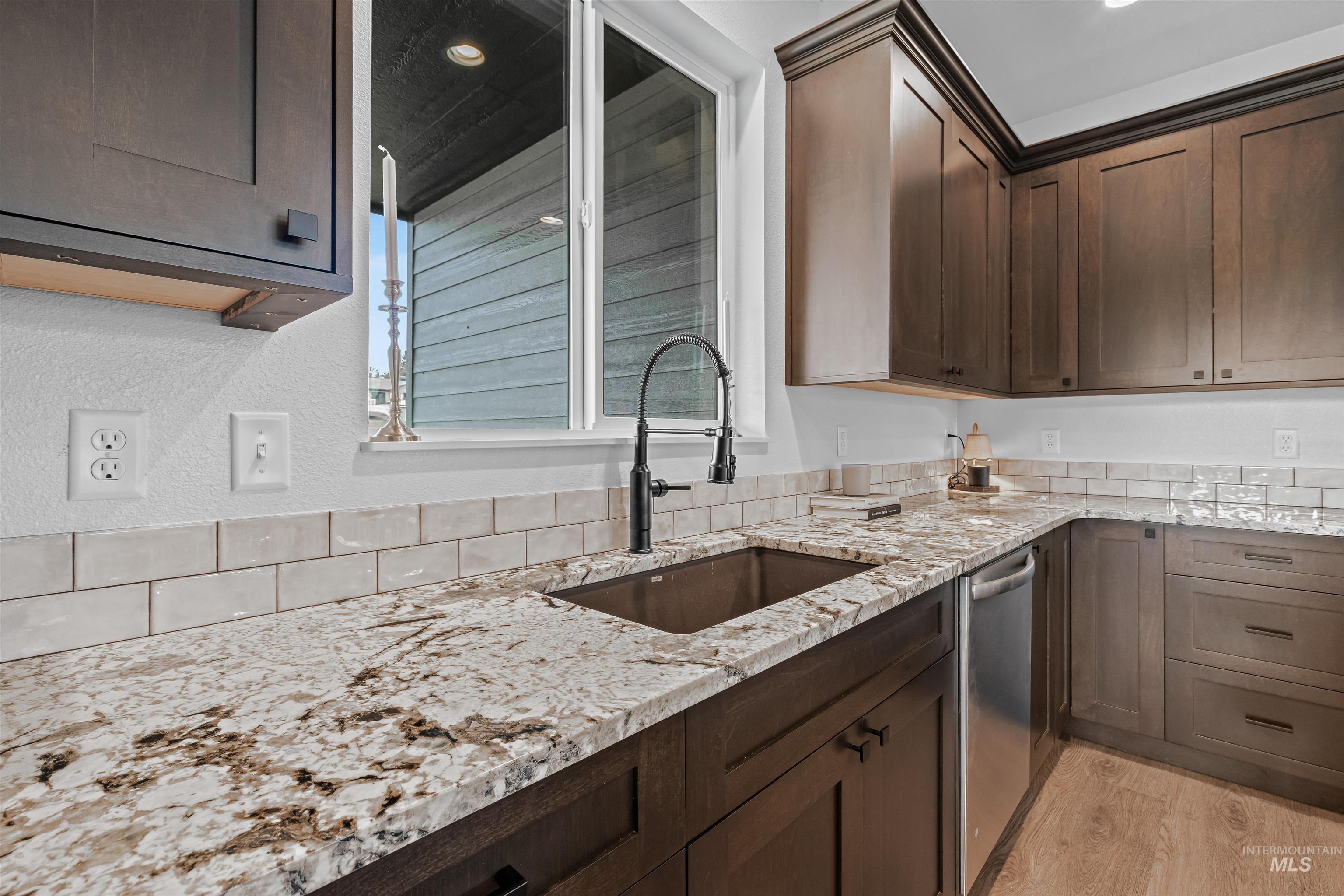 Kitchen with dark brown cabinetry, light stone counters, light wood finished floors, and stainless steel dishwasher