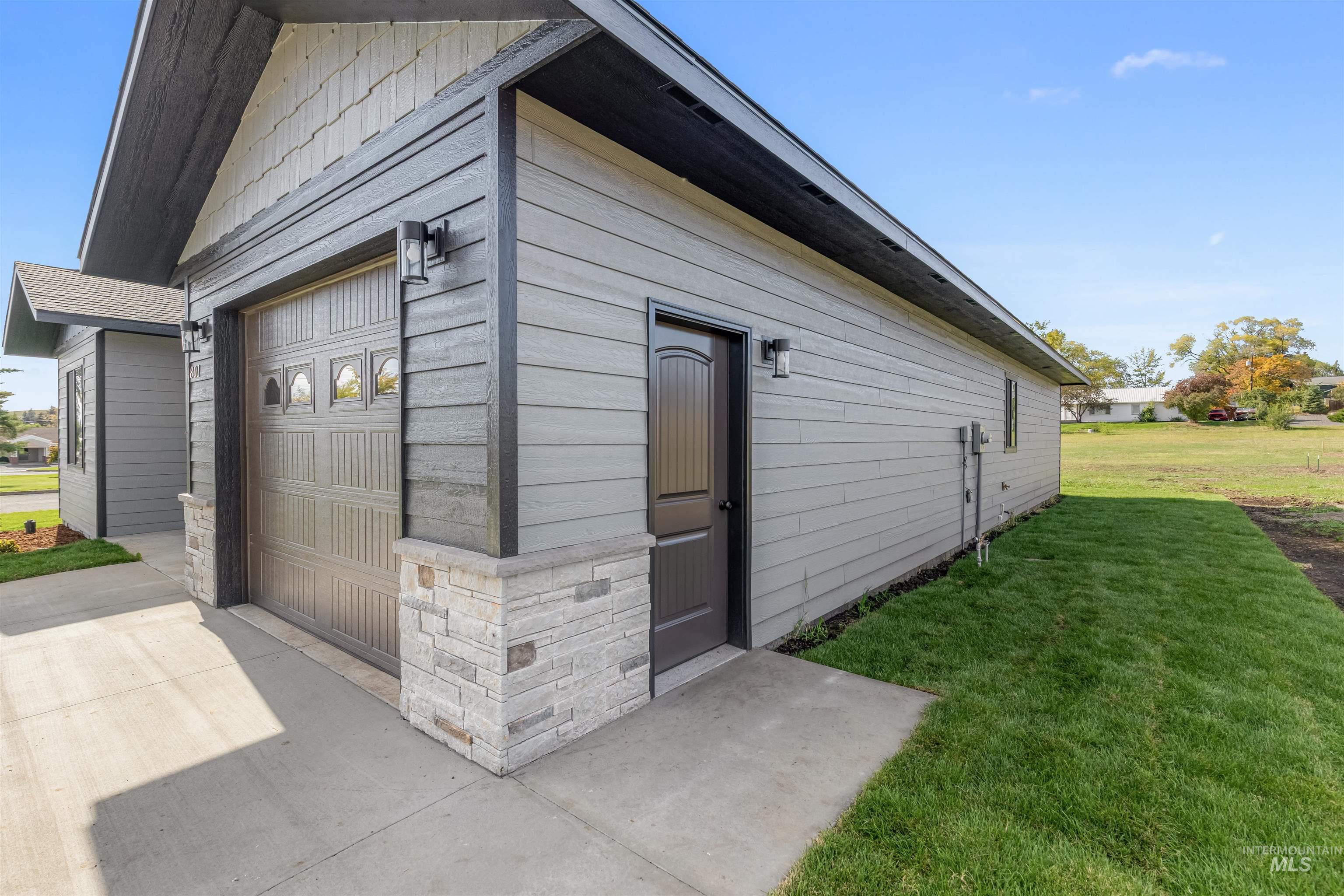 View of side of property featuring a garage, stone siding, a lawn, and concrete driveway