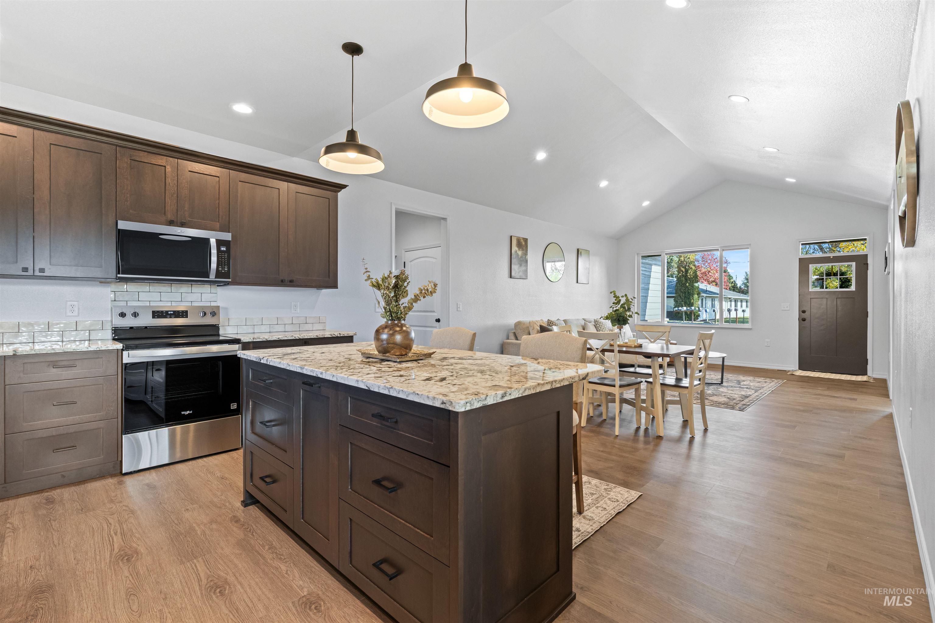 Kitchen with dark brown cabinetry, appliances with stainless steel finishes, decorative backsplash, light stone counters, and decorative light fixtures