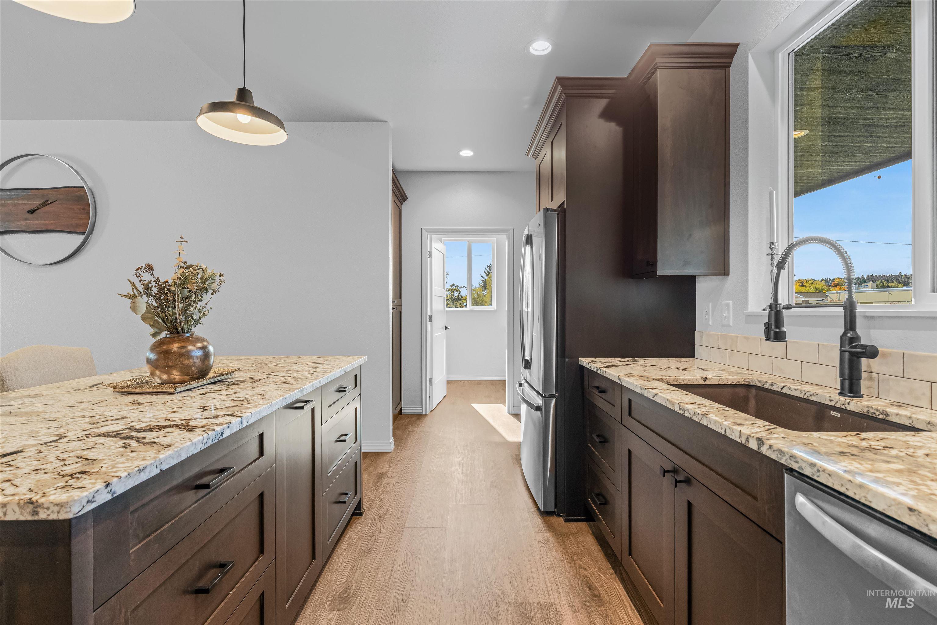 Kitchen with dark brown cabinets, light stone countertops, decorative light fixtures, light wood finished floors, and appliances with stainless steel finishes