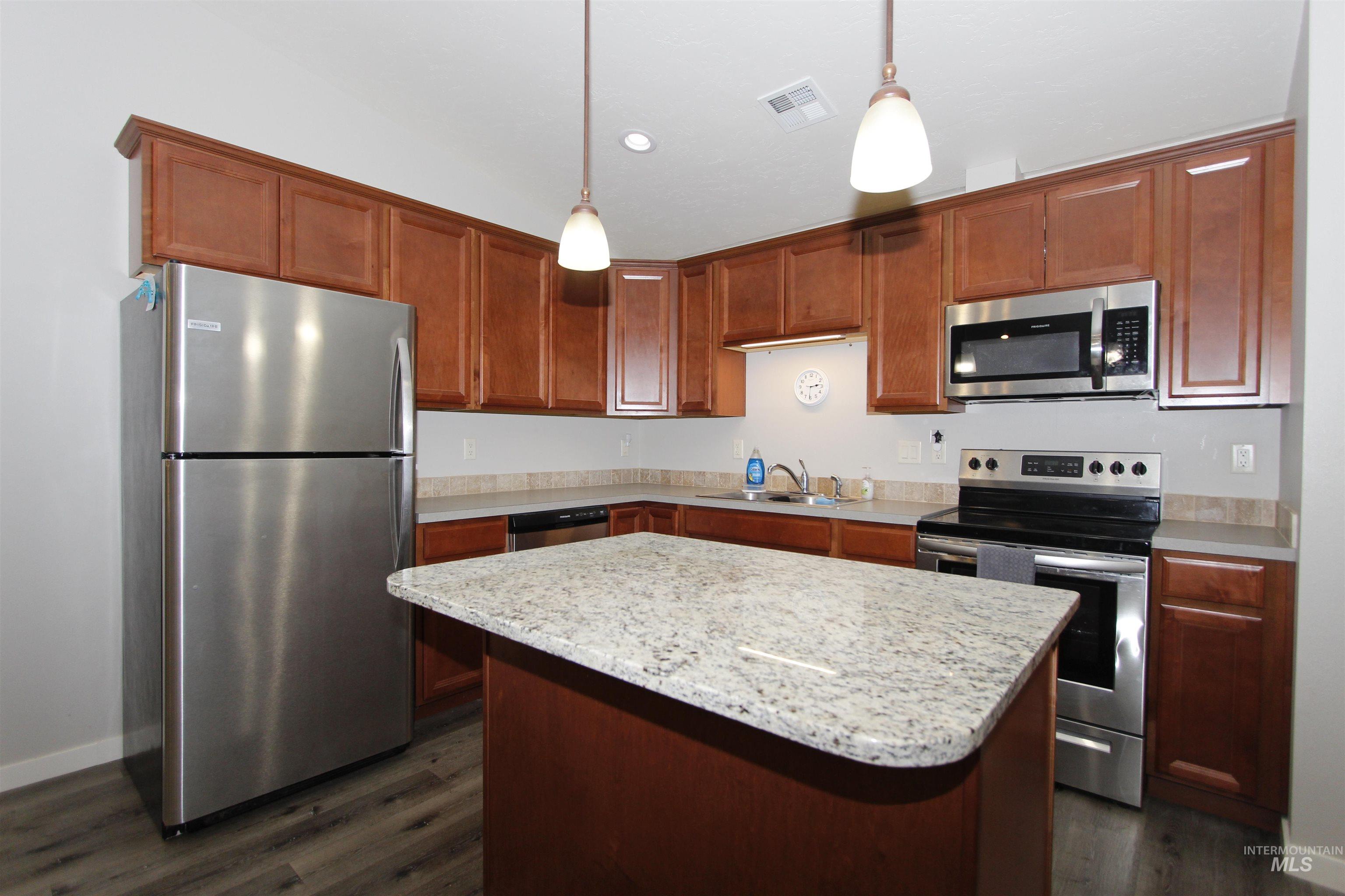 Kitchen with stainless steel appliances, a center island, decorative light fixtures, dark wood finished floors, and recessed lighting