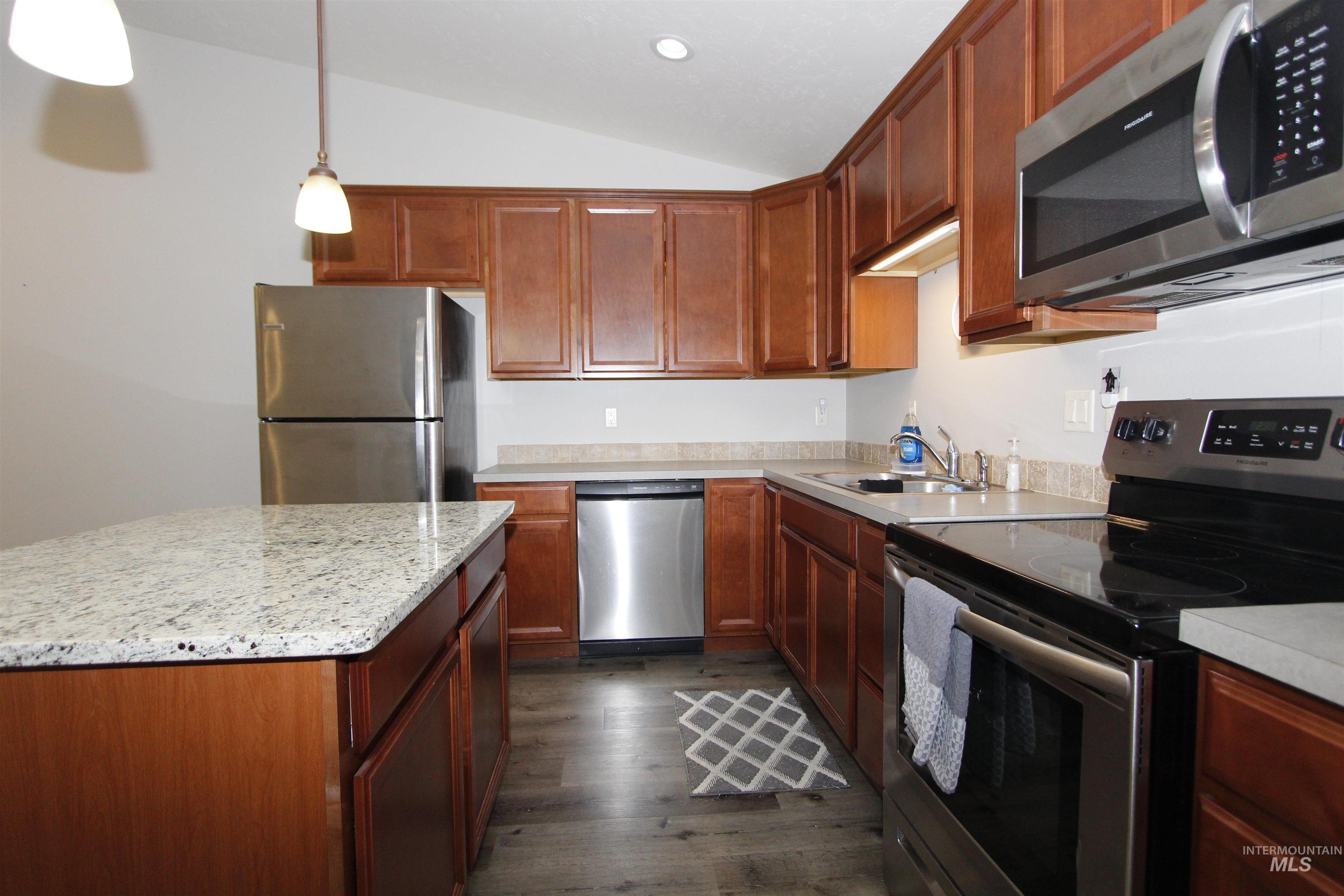 Kitchen featuring appliances with stainless steel finishes, vaulted ceiling, dark wood-style floors, hanging light fixtures, and a center island