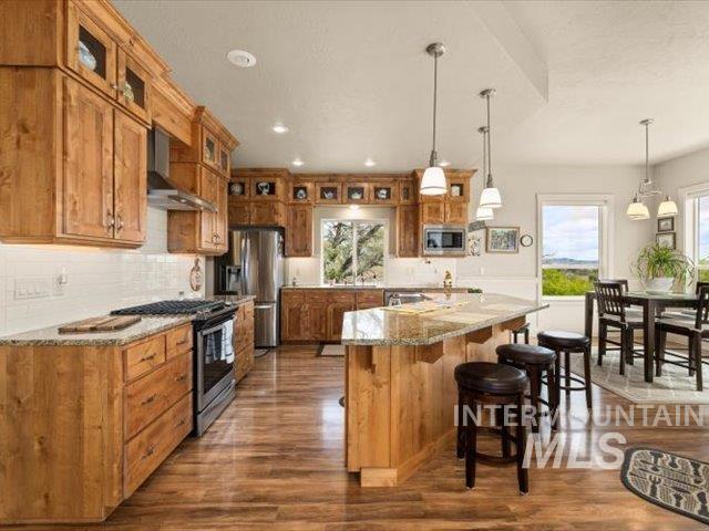 Kitchen featuring brown cabinetry, decorative backsplash, glass insert cabinets, pendant lighting, and stainless steel appliances