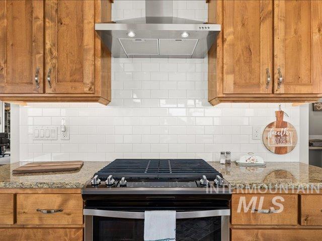 Kitchen with gas range, brown cabinetry, wall chimney exhaust hood, decorative backsplash, and light stone countertops