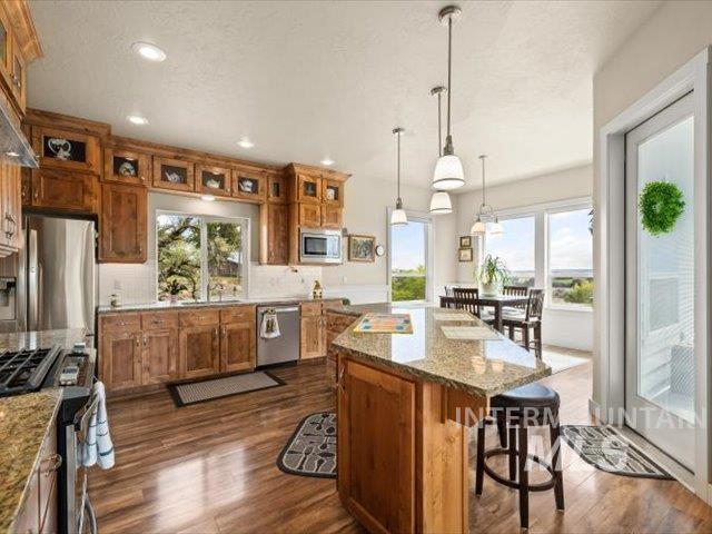Kitchen featuring brown cabinets, decorative backsplash, dark wood-style flooring, decorative light fixtures, and healthy amount of natural light