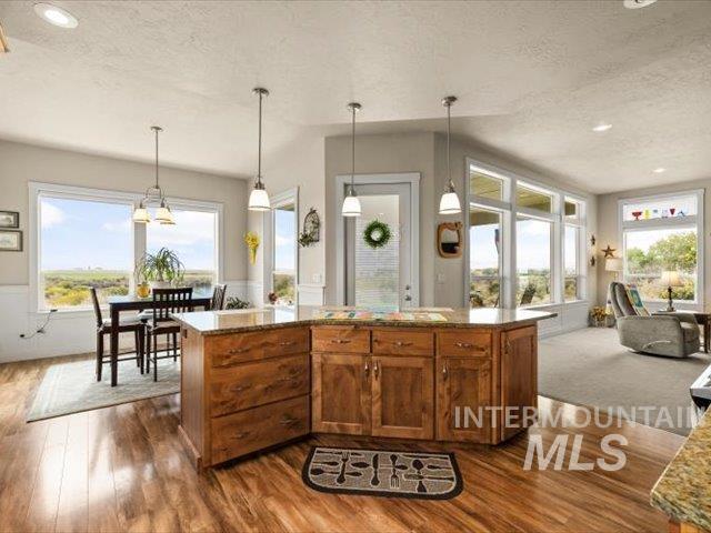 Kitchen featuring pendant lighting, brown cabinetry, recessed lighting, light stone countertops, and healthy amount of natural light
