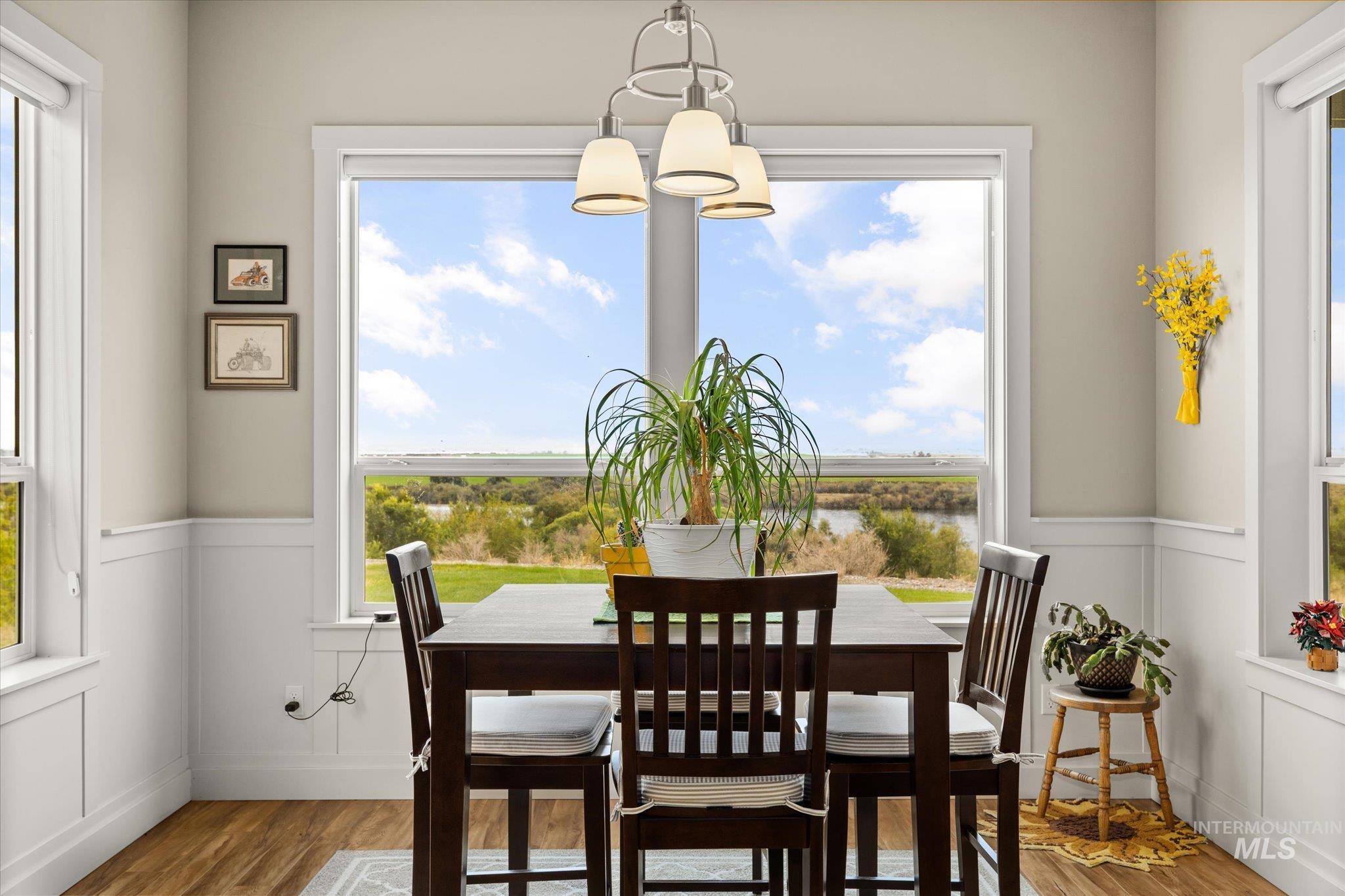 Dining area featuring a decorative wall, wainscoting, healthy amount of natural light, wood finished floors, and a chandelier