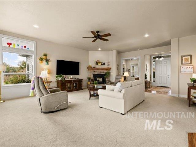 Carpeted living area with a fireplace with raised hearth, recessed lighting, and ceiling fan