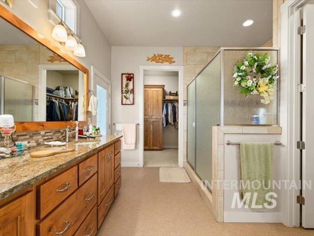 Full bathroom featuring a spacious closet, vanity, a stall shower, and recessed lighting