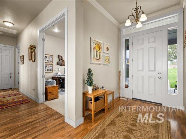 Foyer with wood finished floors, a chandelier, and crown molding