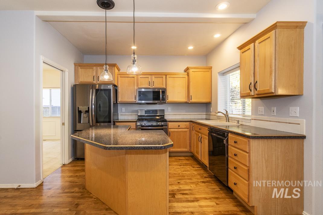 Kitchen featuring pendant lighting, stainless steel appliances, a kitchen island, dark stone countertops, and light wood finished floors