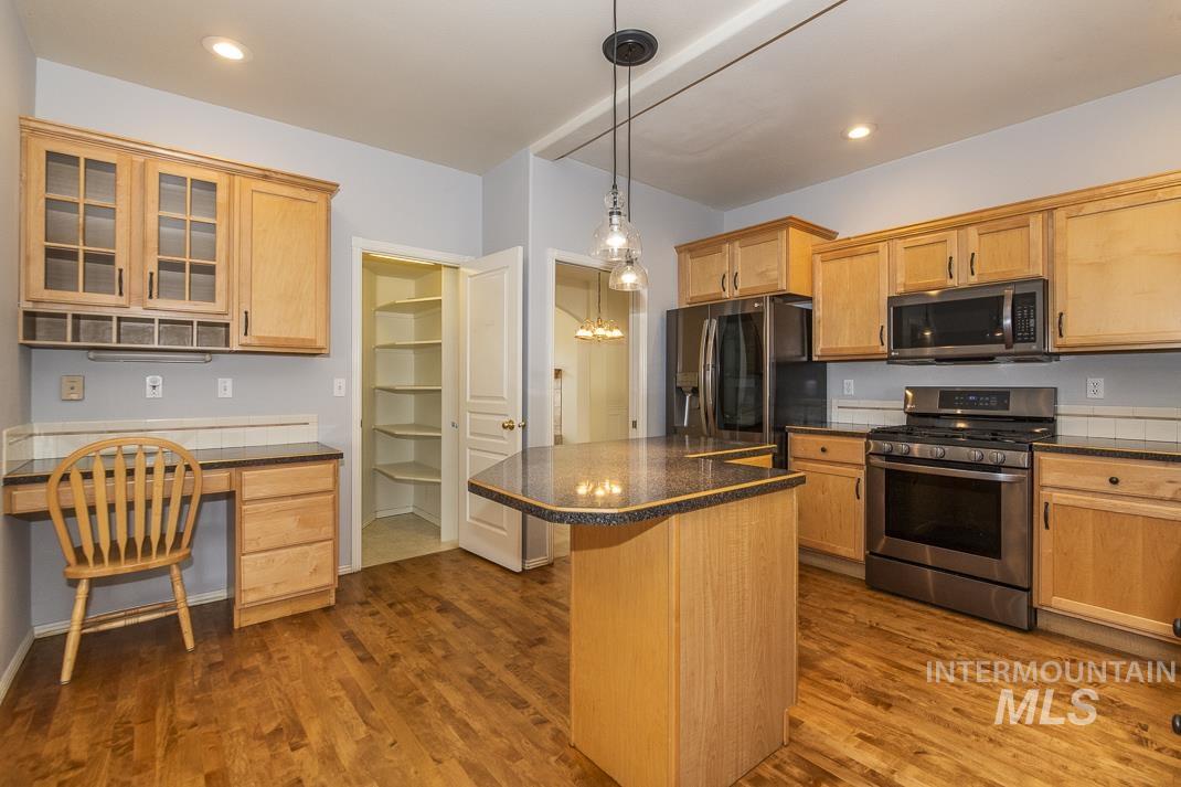 Kitchen with appliances with stainless steel finishes, dark wood-style flooring, glass insert cabinets, a kitchen island, and recessed lighting