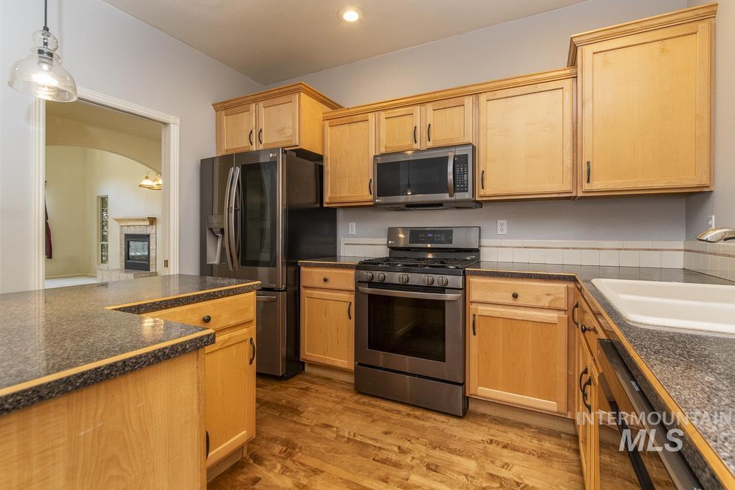 Kitchen with appliances with stainless steel finishes, dark wood-style floors, dark countertops, a glass covered fireplace, and decorative light fixtures