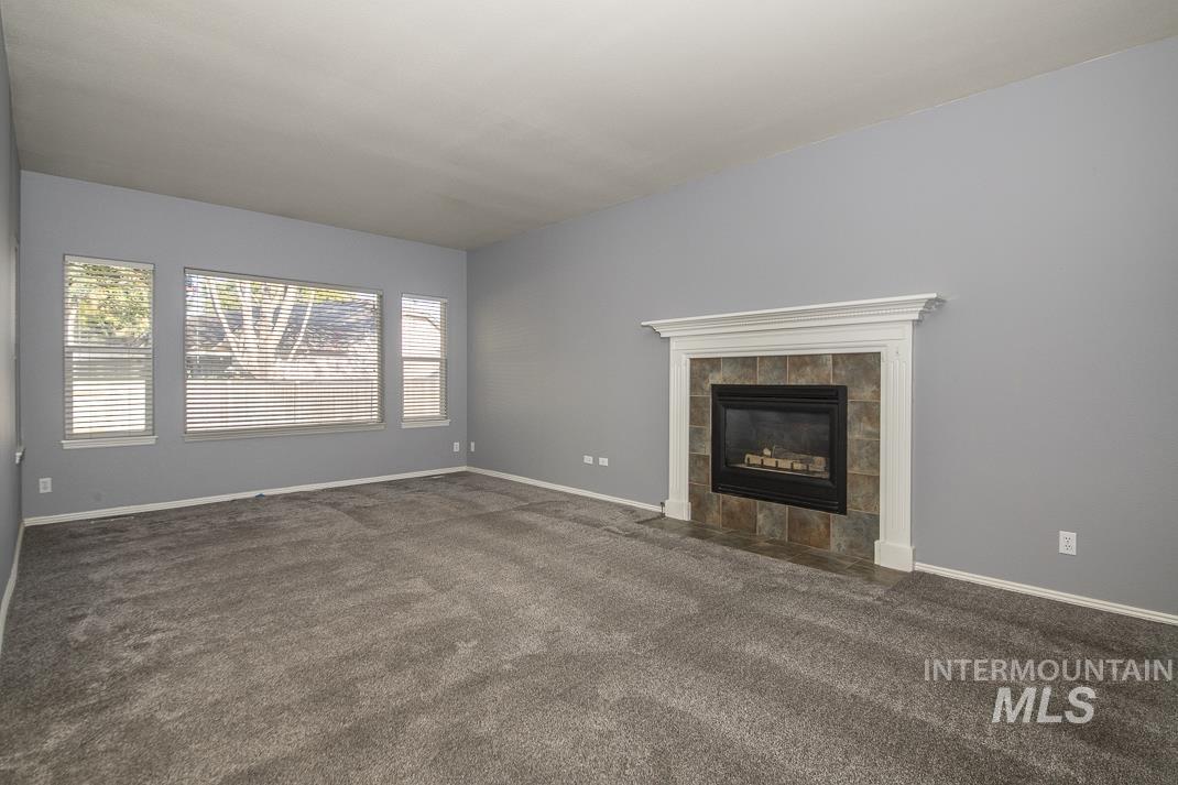 Unfurnished living room with dark colored carpet and a tiled fireplace
