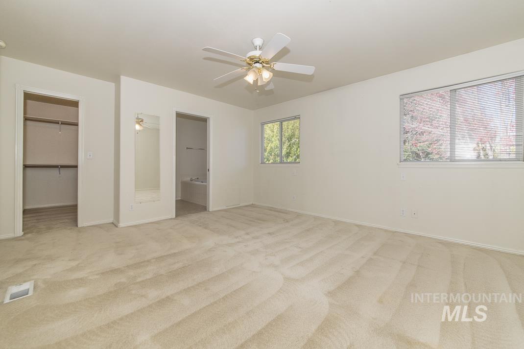 Unfurnished bedroom with light carpet, connected bathroom, a spacious closet, and a ceiling fan