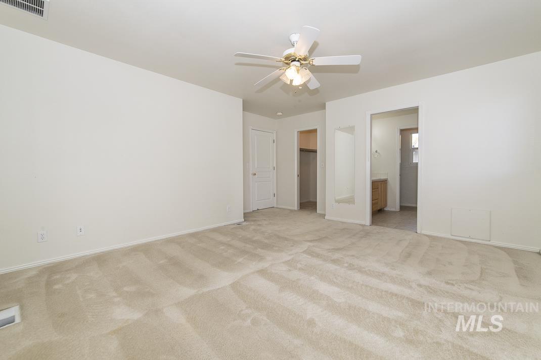 Unfurnished bedroom featuring a walk in closet, light colored carpet, a ceiling fan, and ensuite bathroom