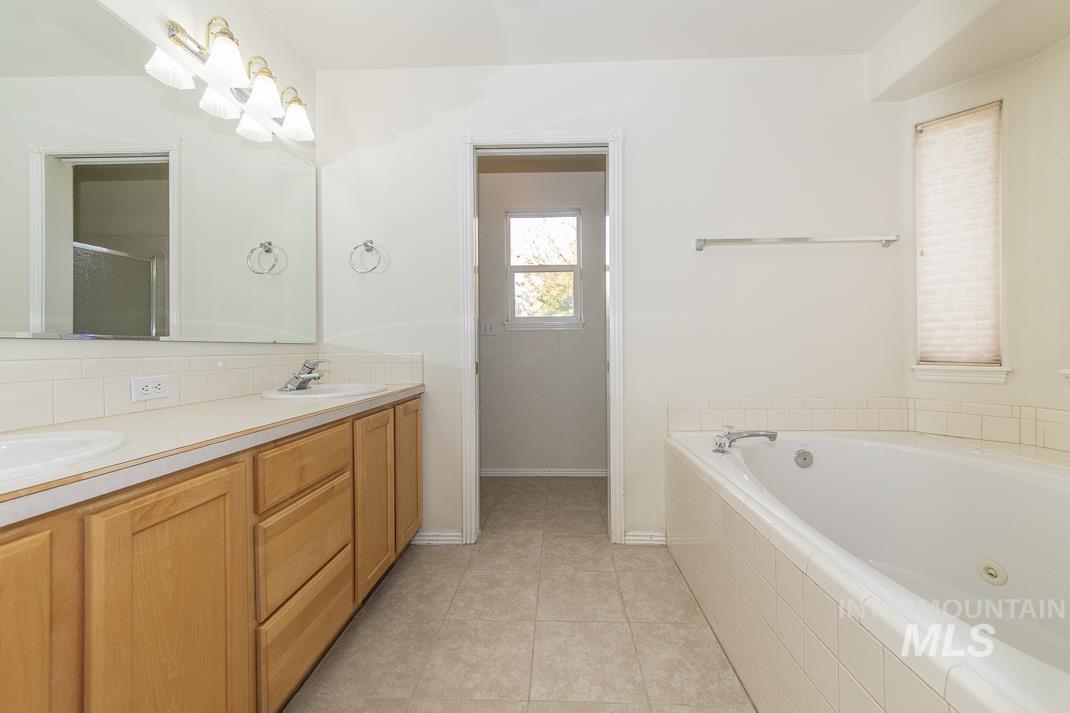 Full bathroom featuring double vanity, a whirlpool tub, light tile patterned floors, and backsplash