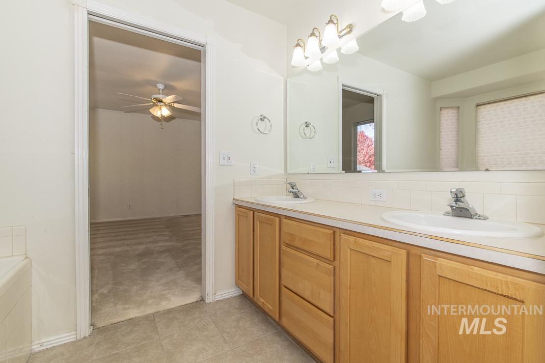 Bathroom with double vanity, light tile patterned flooring, tasteful backsplash, light colored carpet, and a ceiling fan
