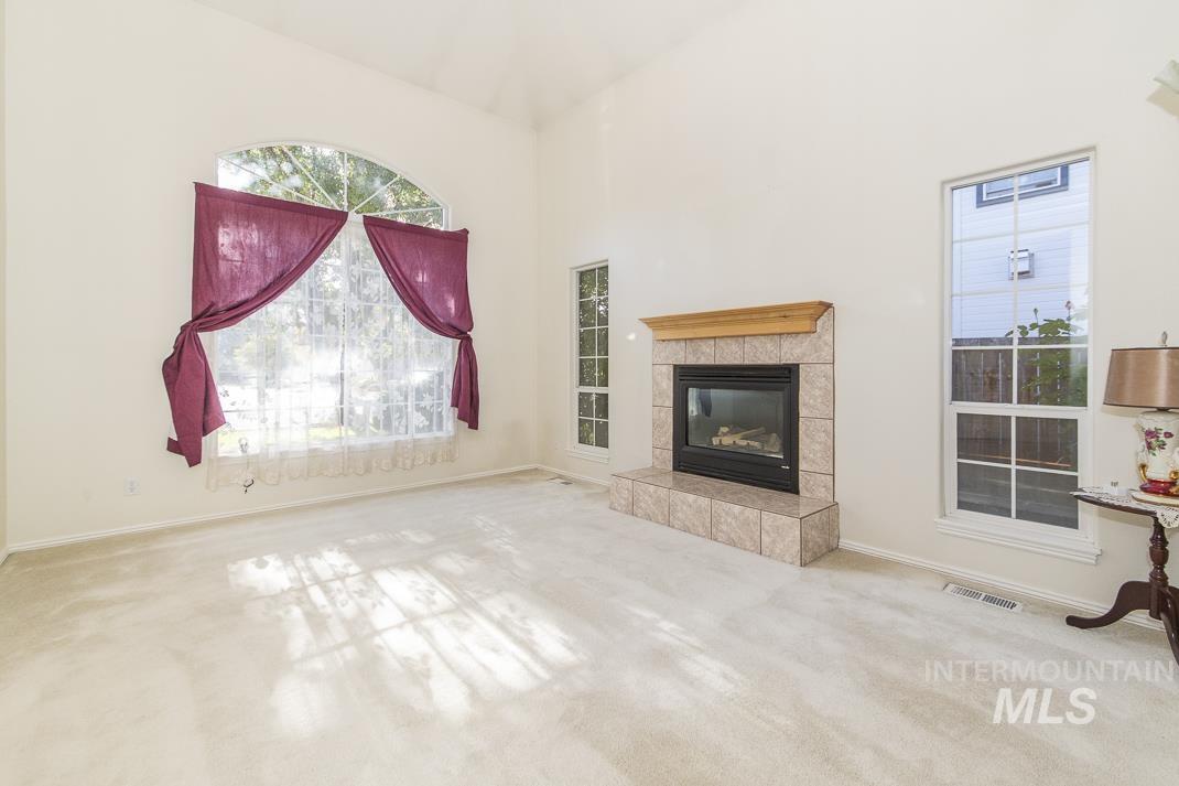 Unfurnished living room featuring light carpet, a tiled fireplace, and a high ceiling