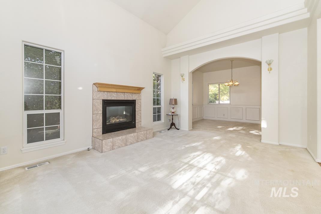 Unfurnished living room with carpet flooring, high vaulted ceiling, a tiled fireplace, and arched walkways